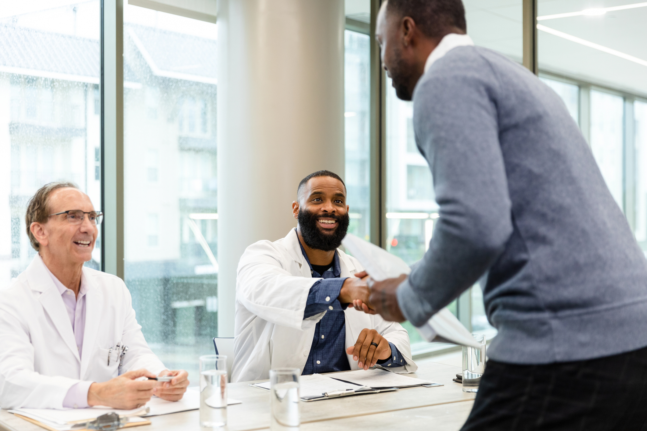 Two male doctors on staff at the hospital greet the unrecognizable male job applicant.